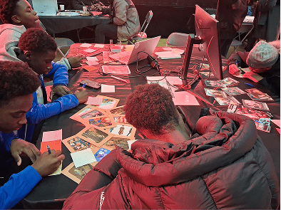 Des jeunes sont assis et travaillent autour d'une table sur laquelle il y a des cartes et deux ordinateurs